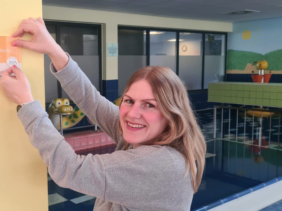 Marketingleiterin Carolin Ewen bringt die Plakette Kinderferienland Niedersachsen im Bad an.