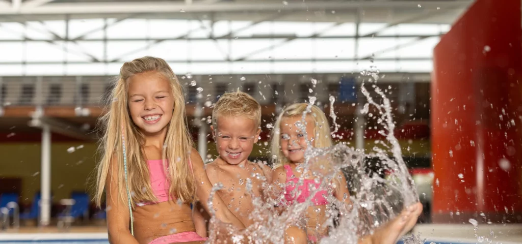 drei Kinder sitzen am Beckenrand und planschen im Wasser