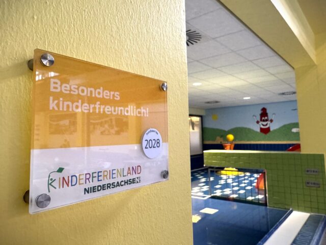 Schild zur Zertifizierung der Auszeichnung "Kinderferienland Niedersachsen" mit dem Kleinkindbecken im Hintergrund