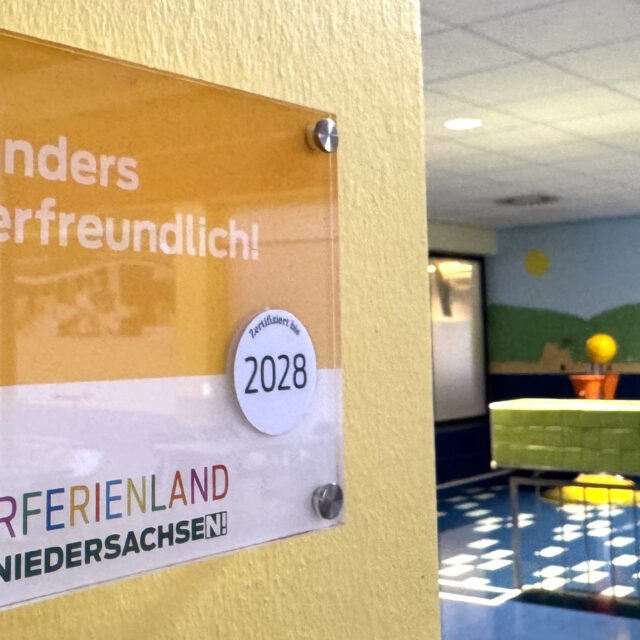 Schild zur Zertifizierung der Auszeichnung "Kinderferienland Niedersachsen" mit dem Kleinkindbecken im Hintergrund