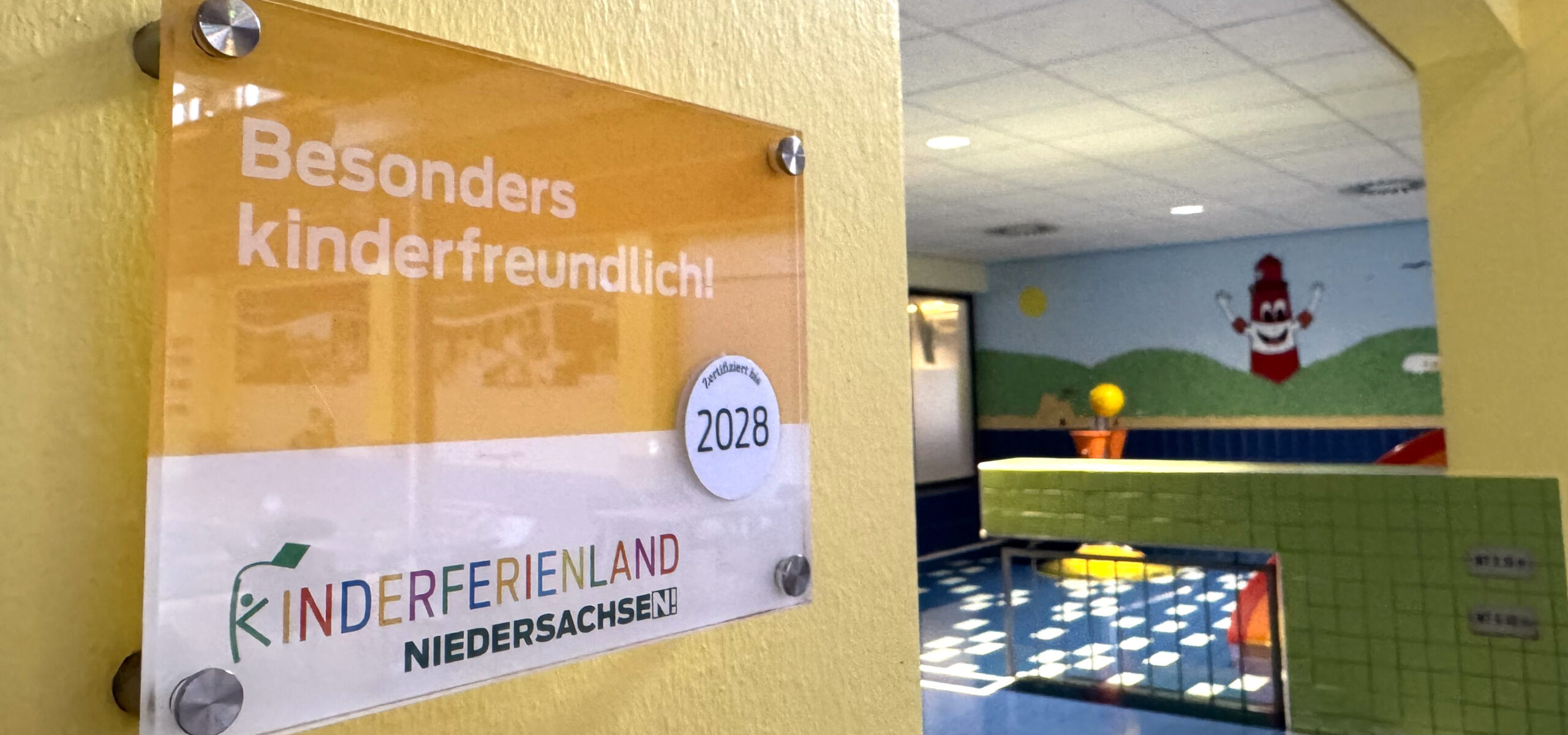 Schild zur Zertifizierung der Auszeichnung "Kinderferienland Niedersachsen" mit dem Kleinkindbecken im Hintergrund
