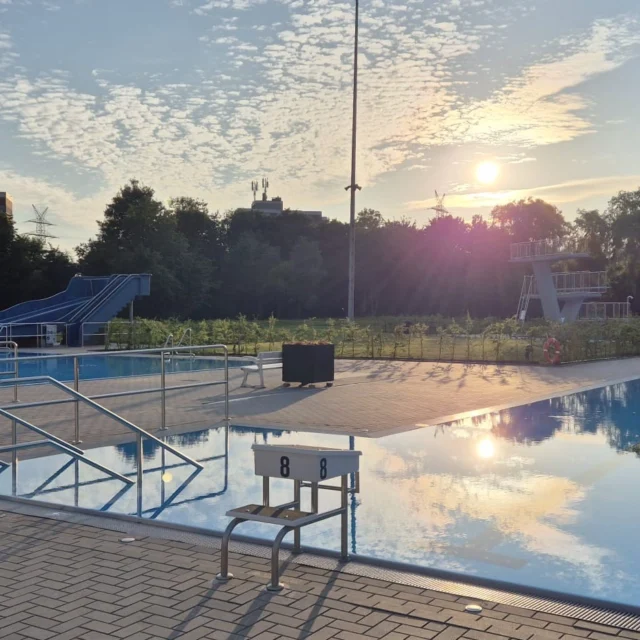Blick auf beide Schwimmbecken mit Rutsche und Sprungturm im Hintergrund.