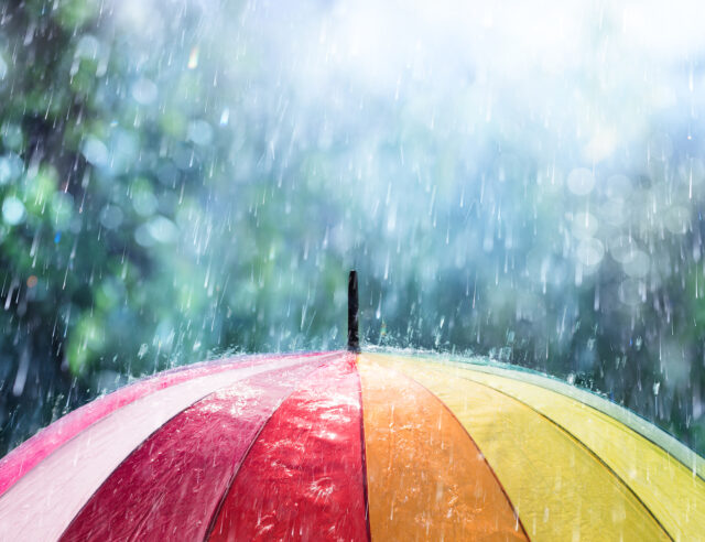 Regentropfen fallen auf einen bunten Regenschirm