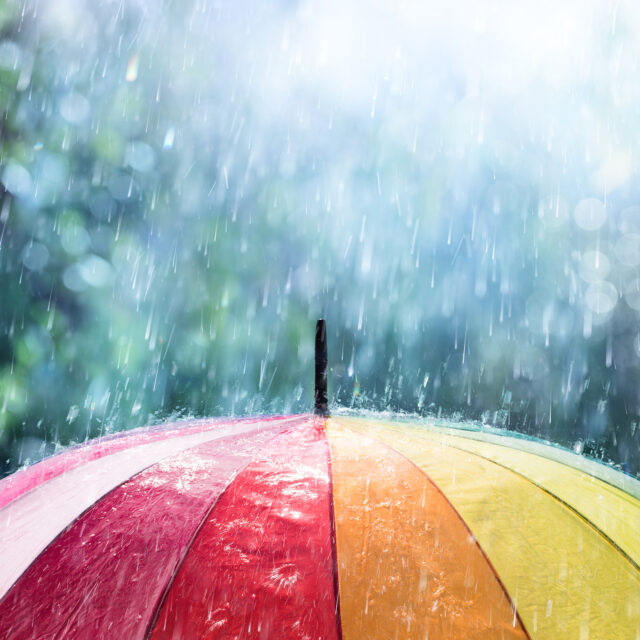 Regentropfen fallen auf einen bunten Regenschirm