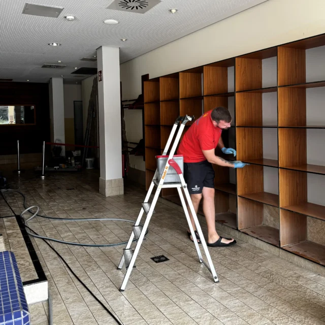 Eine Person wischt Regale ab. Einige Regale sind noch mit Baustaub durch die Baustelle bedeckt.