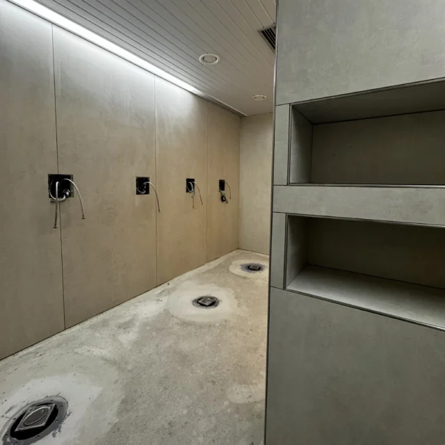 Blick in den Duschraum. Die Wände und der Raumtrenner mit Ablagefächern sind gefliest.