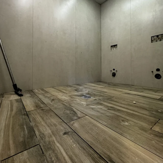 Blick in den Toilettenraum. Die Bodenfliesen sind verlegt. An einer Wand sind Anschlüsse für Toilette und Spülung zu sehen.