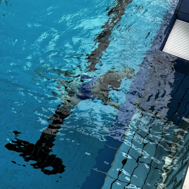 Eine Person schwimmt unter Wasser am Beckenrand.